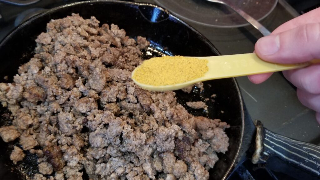 dumping taco seasoning into skillet of meat for taco salad recipe