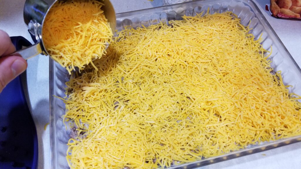 dumping cheese into baking dish for tater tot casserole