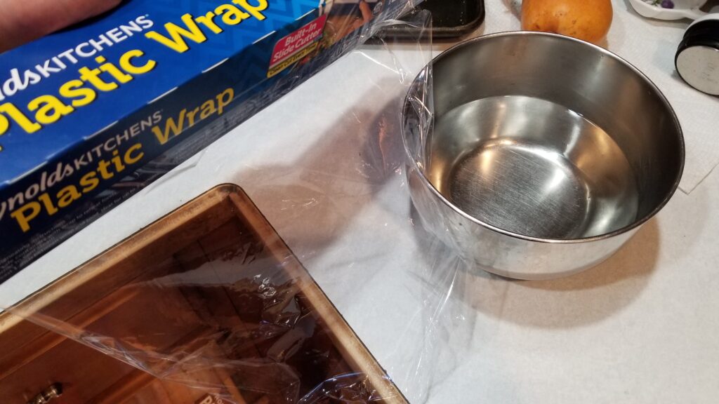 putting cling wrap on bowl of vodka and water for Jello shot recipe
